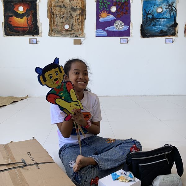 A smiling girl holding up the wayang puppet she just made