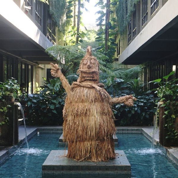 A towering straw guardian standing in a courtyard pool
