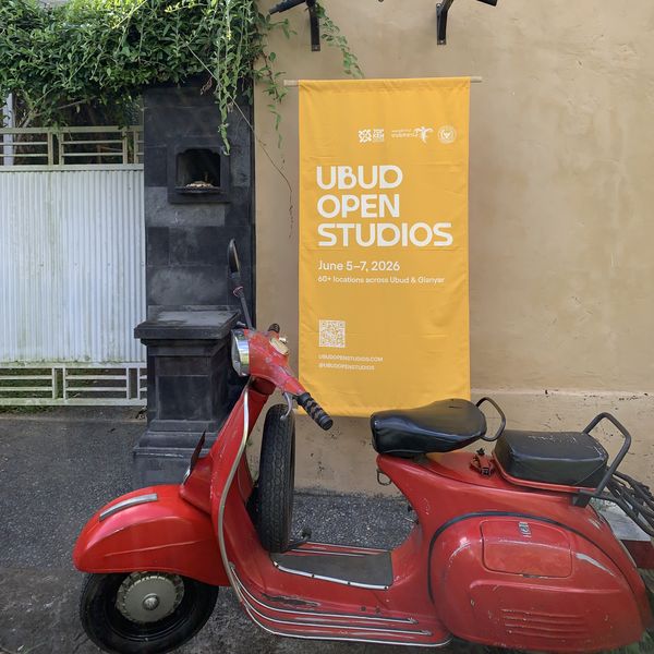 An Ubud Open Studios 2026 banner hanging on a yellow wall above a red vintage scooter