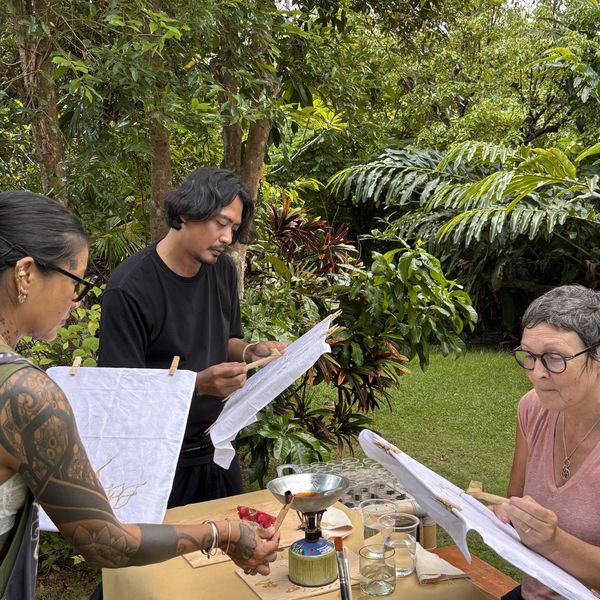 Guests drawing wax designs on batik cloth around a table in a lush Ubud garden