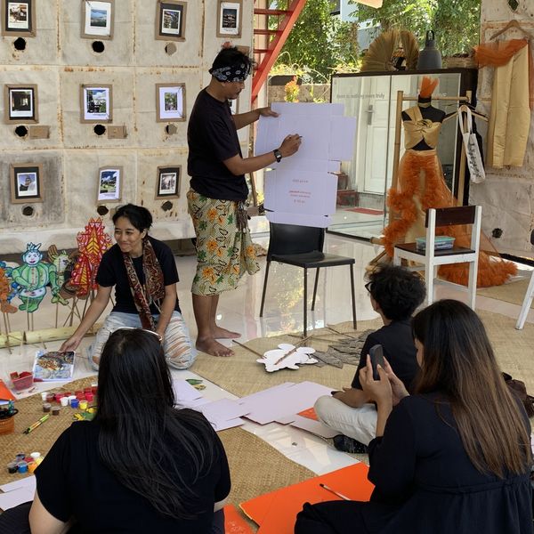 Our artist sketches a wayang design on a board while participants paint on woven mats at Kitapoleng